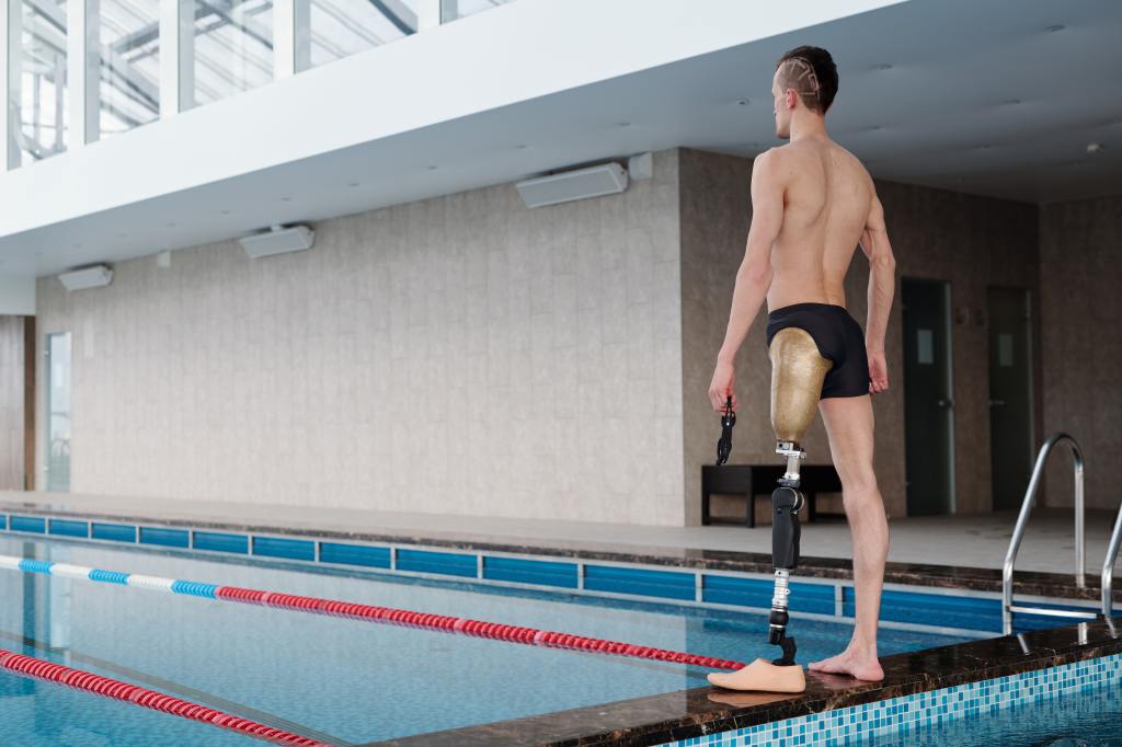 Männlicher Anwender im Schwimmbad mit Oberschenkelprothese in Badehose am Beckenrand